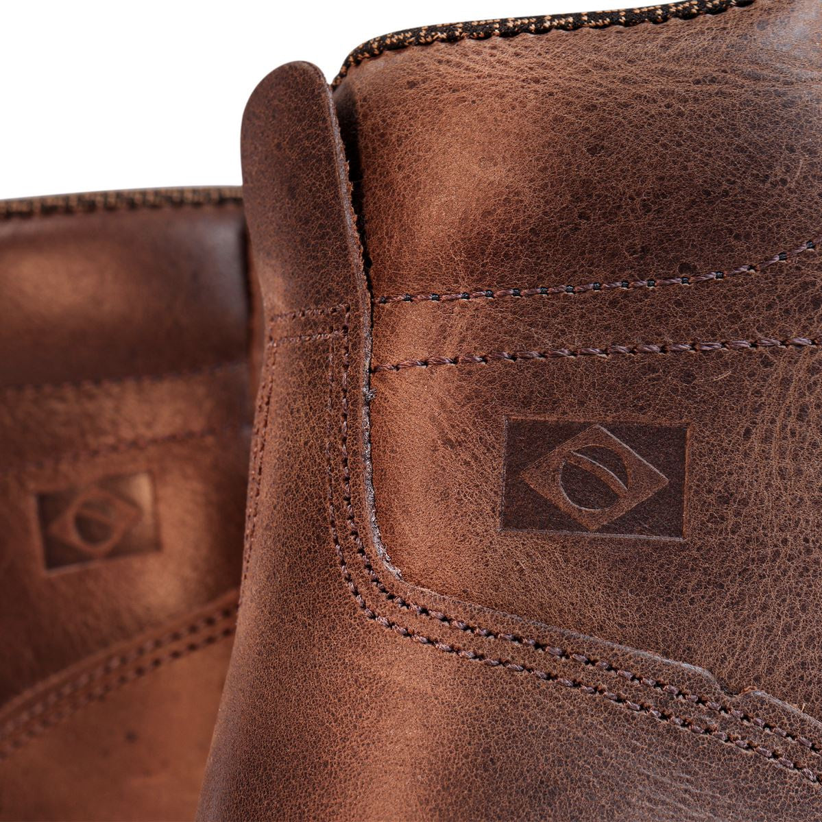 Detalhe em couro marrom com costura reforçada e logo gravado a quente